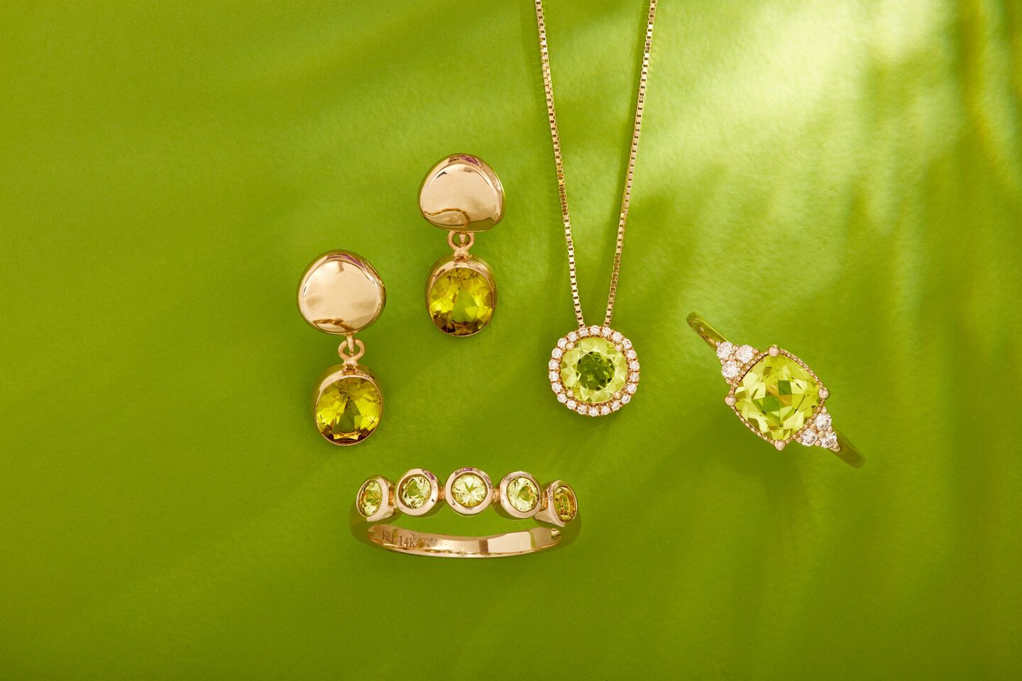 A variety of green gemstone jewelry is shown in 14k yellow gold with a green background. 